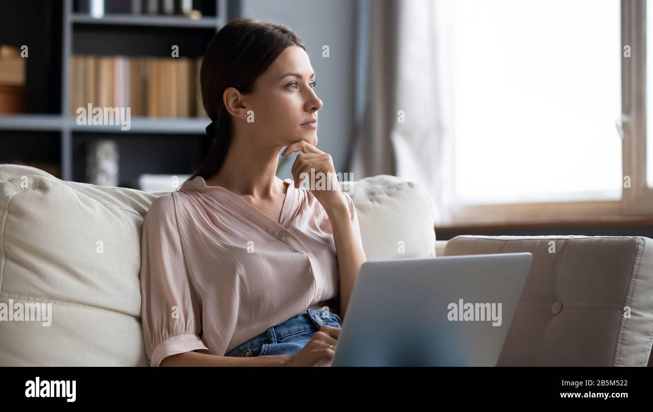 Distracted from work young woman sitting on couch with laptop. Stock Photo