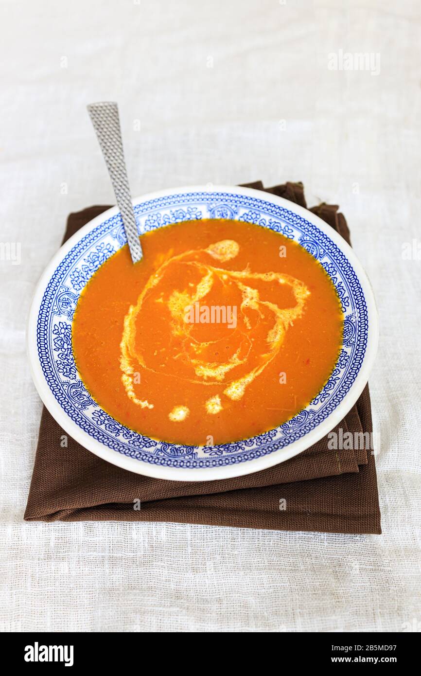Orange pumpkin puree soup with smerana and red chili peppers in a plate with a blue traditional Moroccan pattern on a plain white background. Flat lay Stock Photo