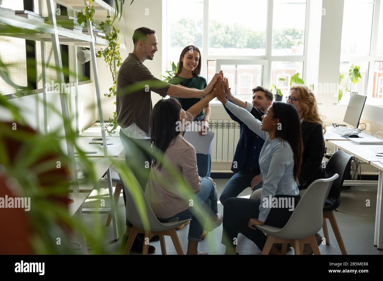Excited multiracial coworkers give high five celebrating success in ...