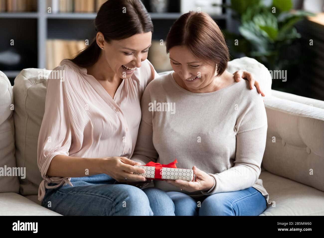 Affectionate elderly senior mom prepared surprise to grownup daughter. Stock Photo