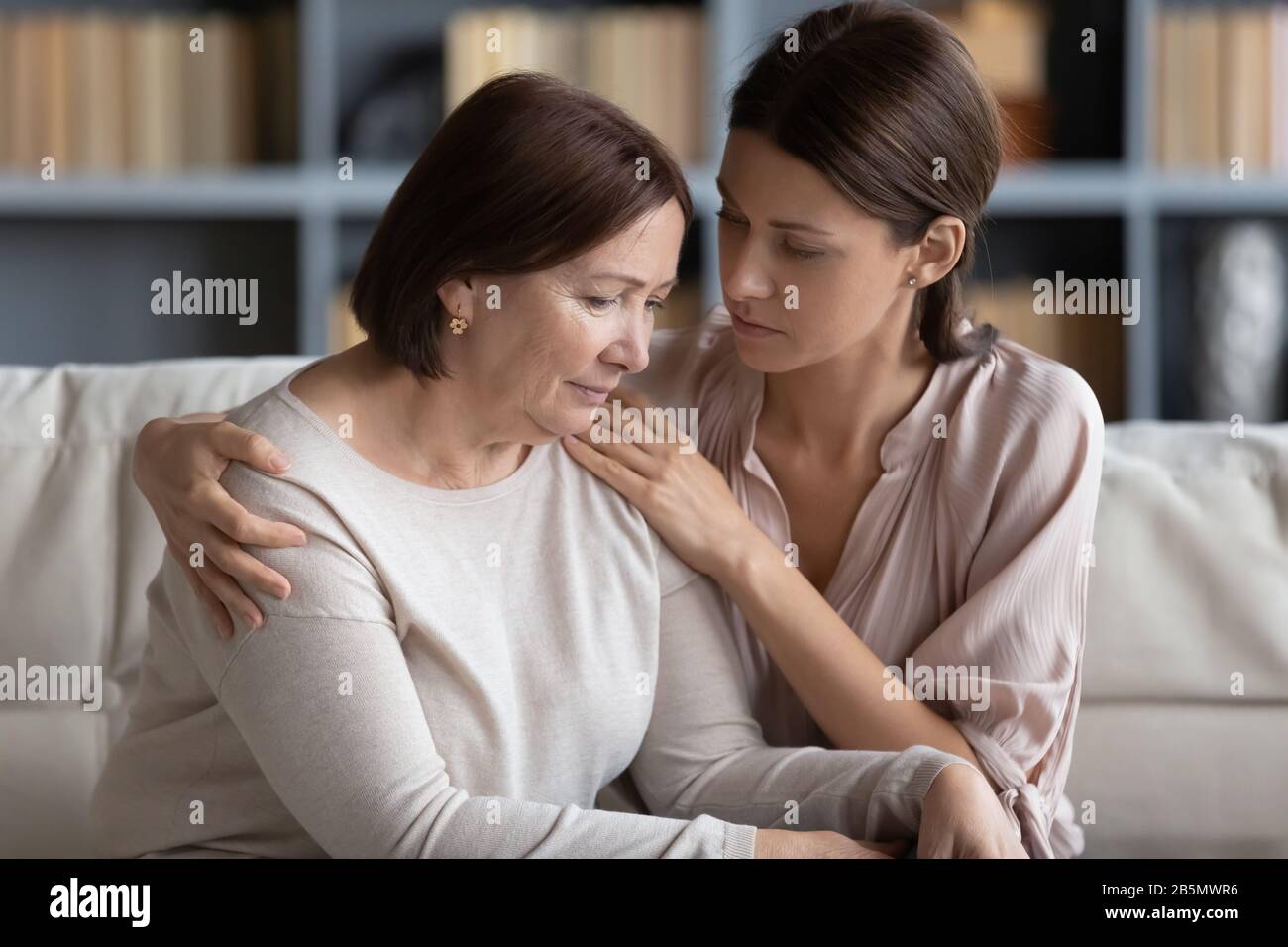 Compassionate woman embracing shoulder of unhappy stressed middle aged mommy. Stock Photo