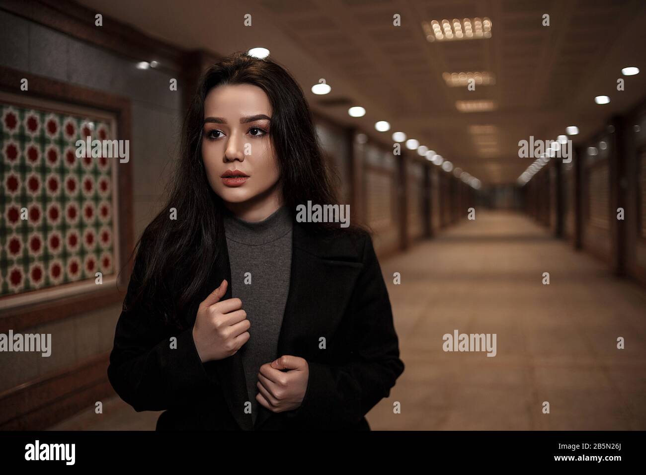 a young beautiful woman walks through an underground passage at night, looking back with fear Stock Photo