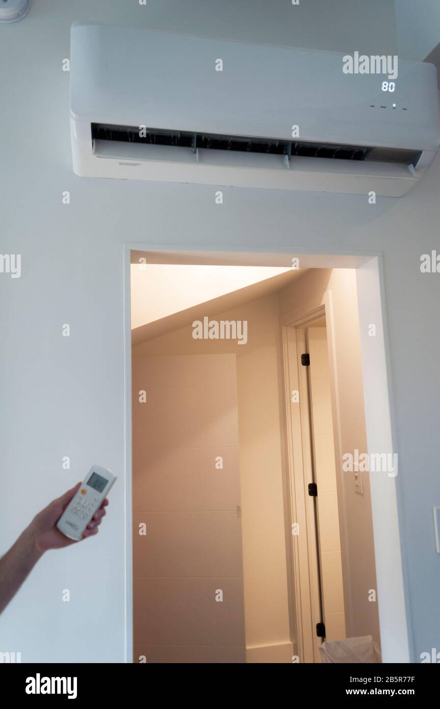 An HVAC unit on the wall shows a temperture of 80 F, set by the remote hand unit. Such heating, ventilation and airconditioning units are very common Stock Photo