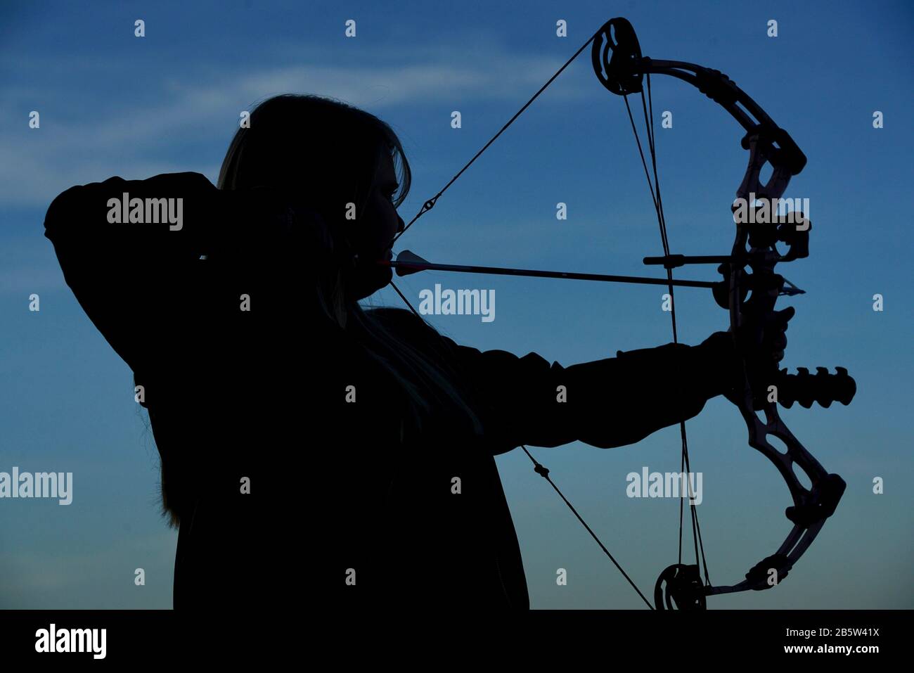 A silhouette of a woman with a bow and arrow doing some archery shooting. Stock Photo