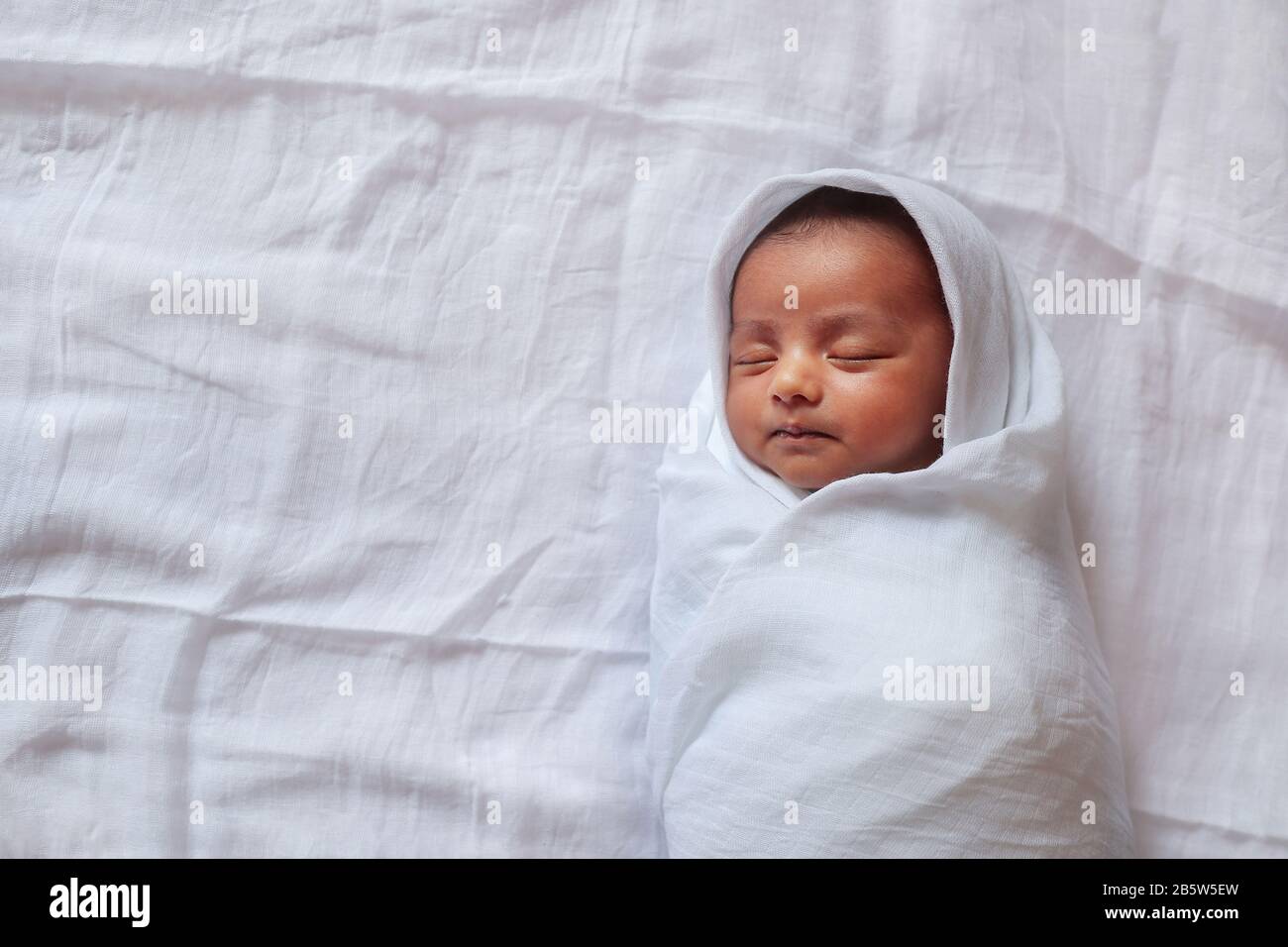 a one month old baby sleeping and swaddled in white cloth lying in