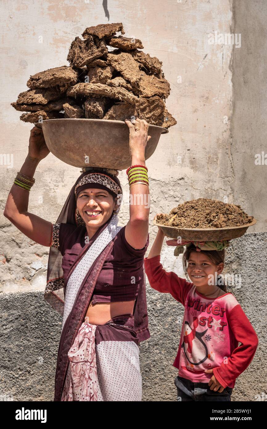 Indian woman and girl carrying basin with cow dung cakes on their heads in Nandgaon. India Stock Photo