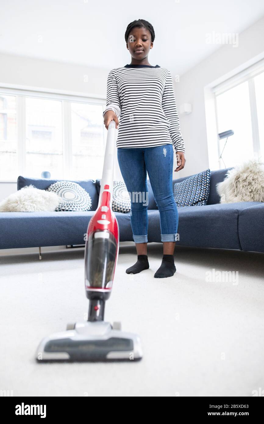 Teenage Girl Helping Out With Chores At Home Vacuuming Carpet In Lounge With Cordless Cleaner Stock Photo