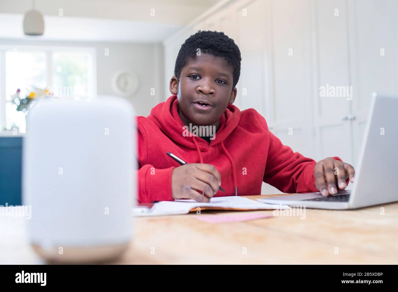 Boy Doing Homework At Home Asking Digital Assistant Question Stock Photo