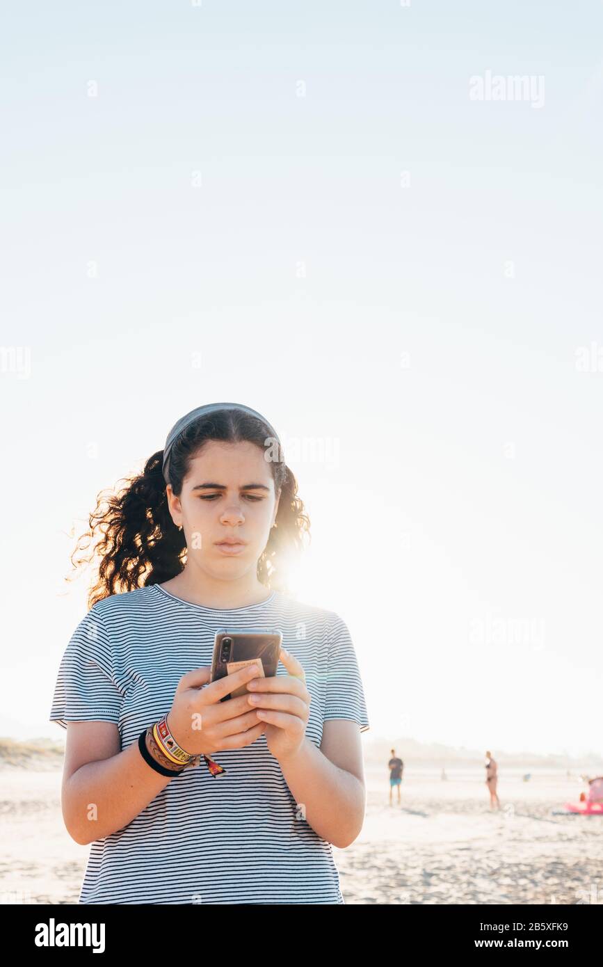 Pretty girl concentrates on reading on her mobile phone at the beach with back light and space for copy Stock Photo