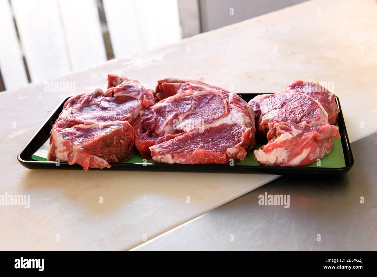 Tray of freshly cut raw chuck steaks on a counter in a butchery or restaurant with copy space below Stock Photo