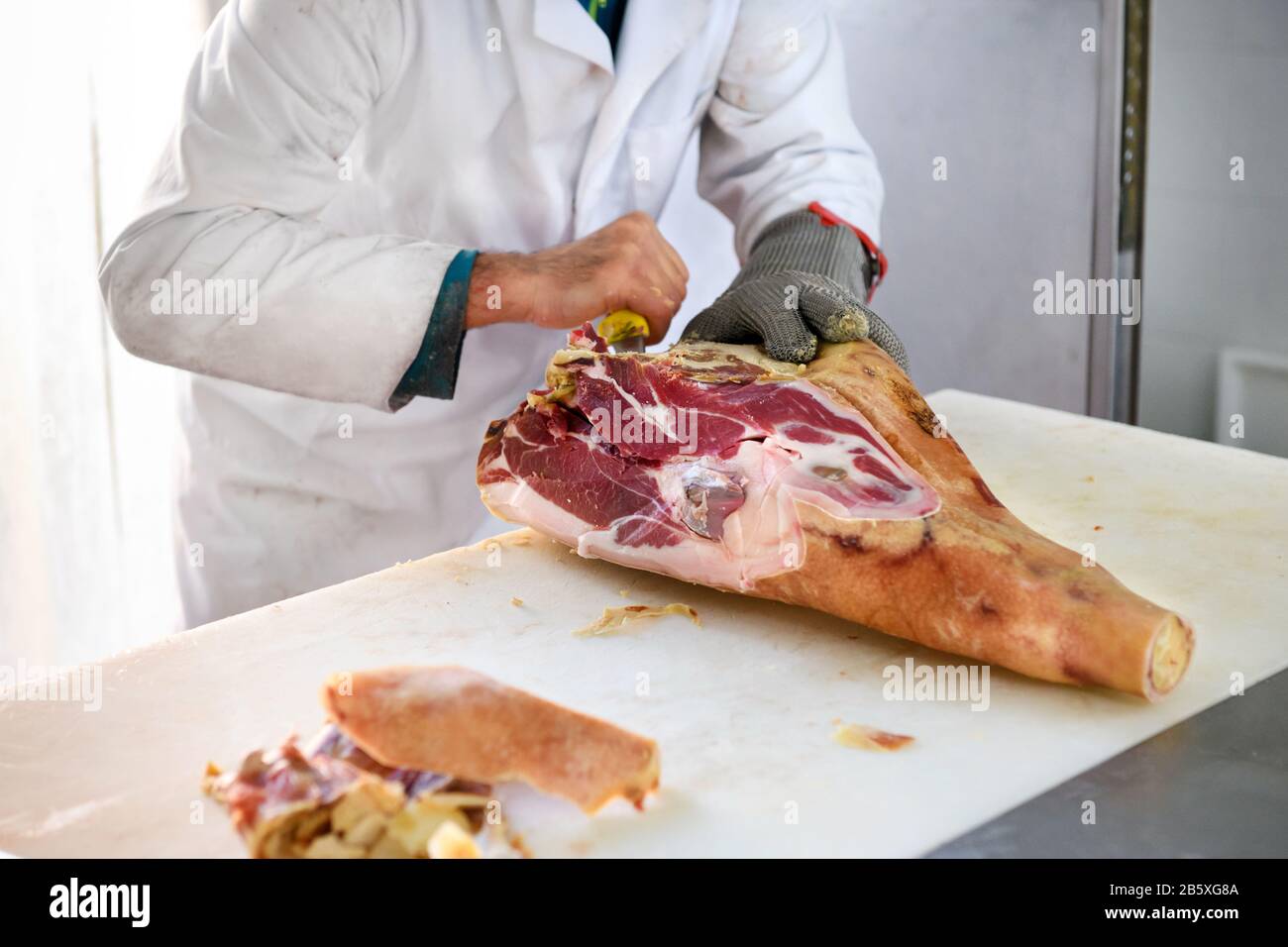 Butcher deboning a leg of Italian dry-cured prosciutto ham on a butchers block with a sharp knife Stock Photo
