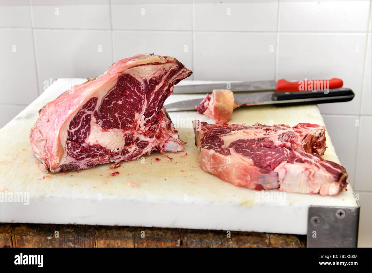 Sliced portion of prime rib eye steak on butchers cutting board with two knives in close up in a butchery Stock Photo