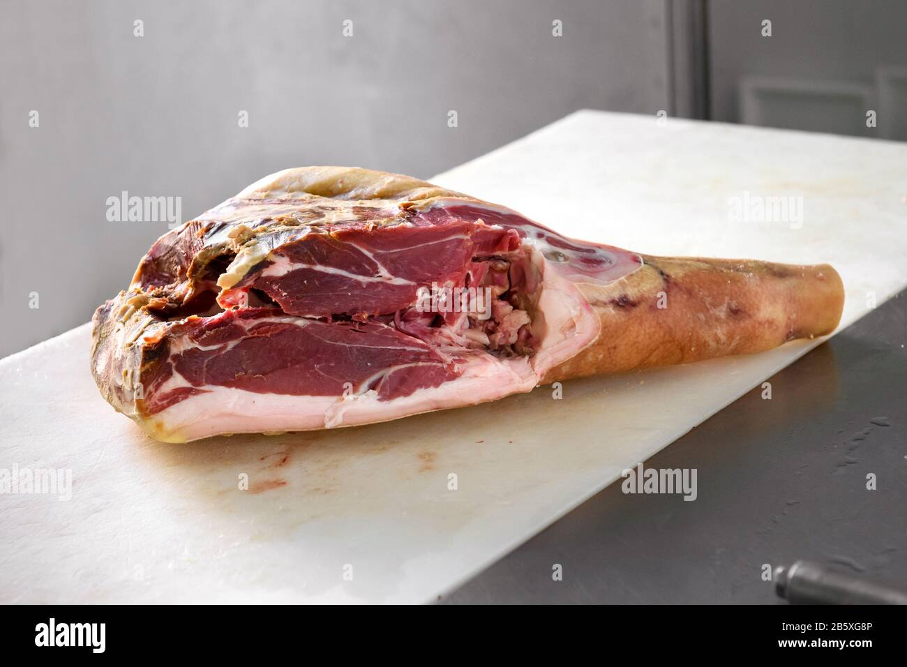 Piece of Prosciutto uncooked ham meat in a butcher shop, viewed in close-up on white cutting table Stock Photo