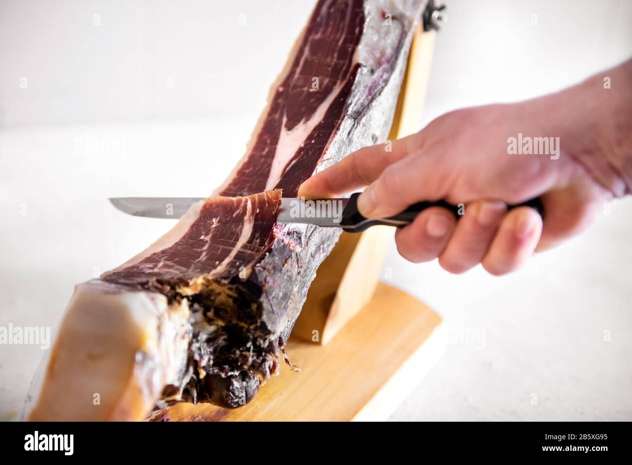 Close-up on male hand slicing Jamon Iberica or Pata Negra Iberian ham from Spain. Cropped view against white background Stock Photo