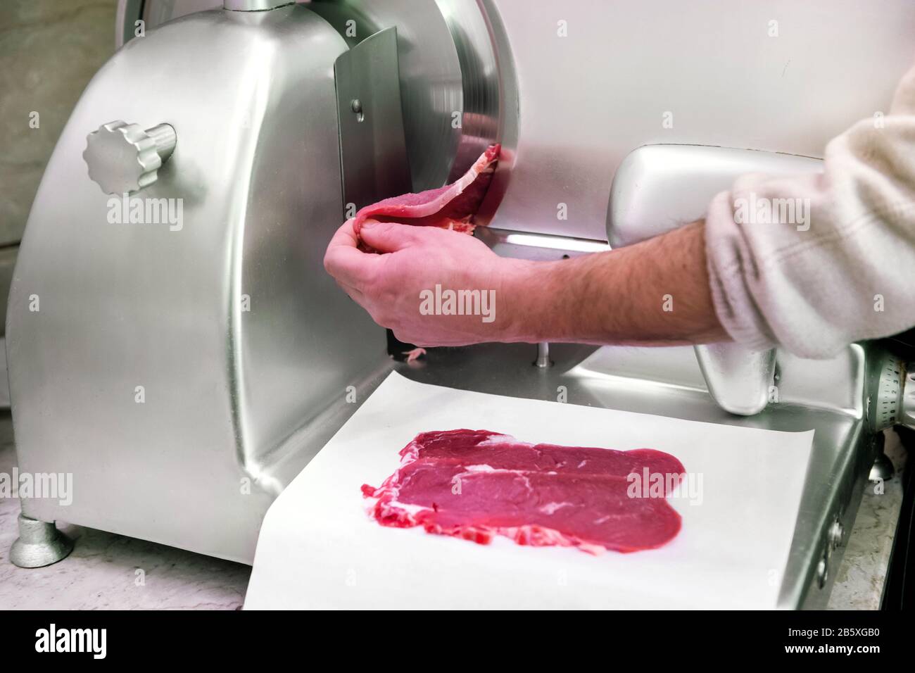 Butcher using a circular blade to slice raw beef steaks laying them neatly on paper below in a close up on his hands and the machine Stock Photo