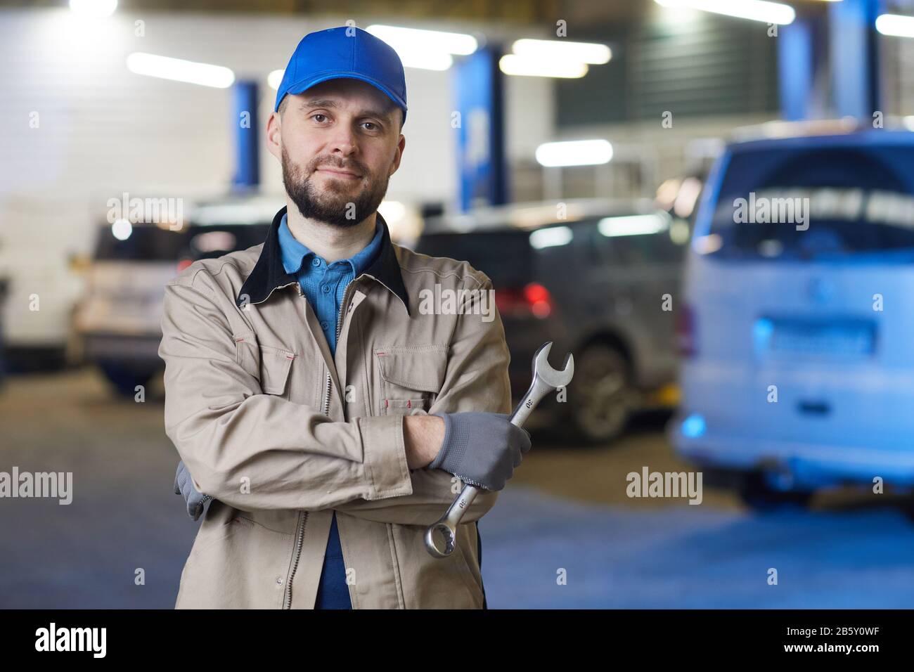 Horizontal waist up portrait of mature Caucasian auto mechanic standing with arms crossed holding spanner looking at camera, copy space Stock Photo