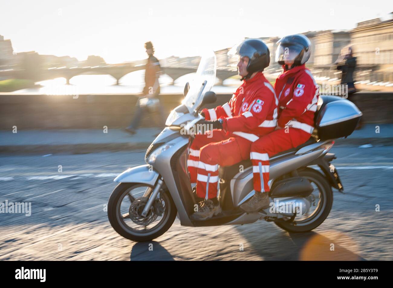 FLORENCE, ITALY - MAY 15, 2012: A pair of emergency response workers ride a scooter across the Arno River. Stock Photo
