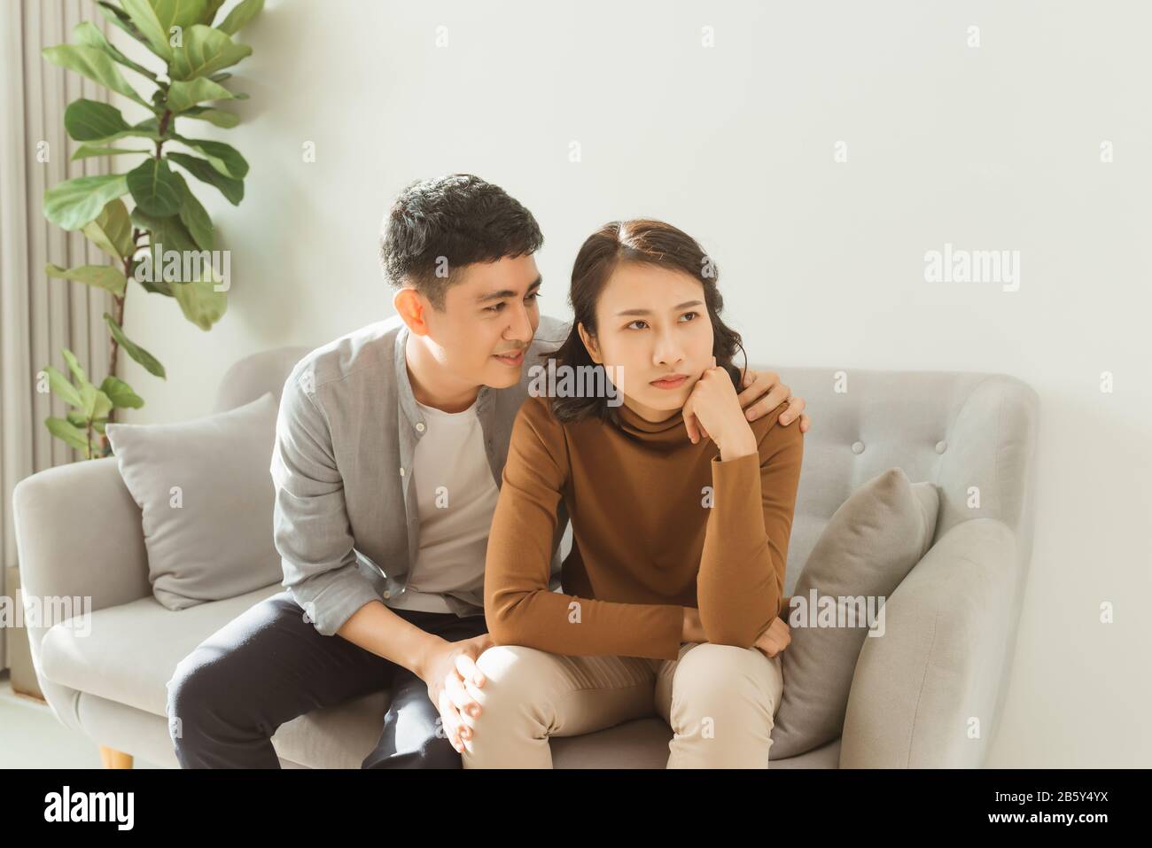 Couple sit on sofa caring wife hugs disappointed sad frustrated husband, making peace, reconcile after fight, problems in relationship, friendship and Stock Photo
