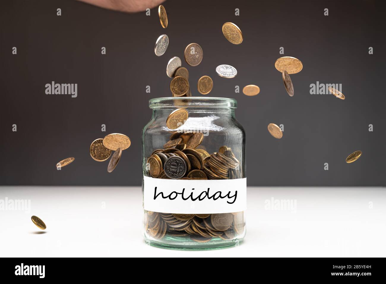 Coins in a jar with holiday text on a white label. Money falling from the sky above. Savings abstract concept. Copy space. Stock Photo