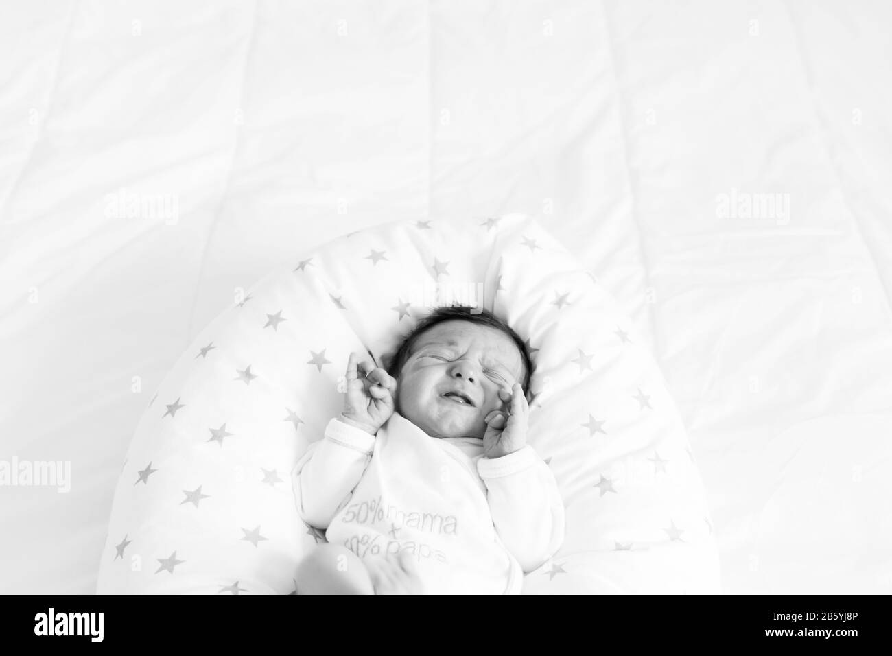 A black and white image of baby crying on a bed Stock Photo
