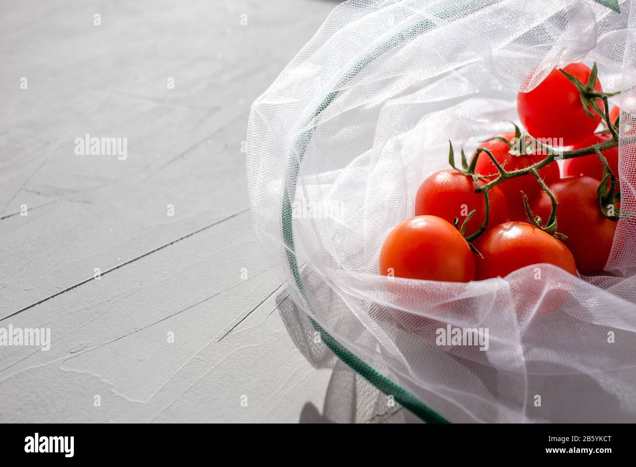 The reusable organza net bag for shopping with tomatoes a grey background.  Concept of no plastic, zero waste, reusable life. Copy space. Stock Photo
