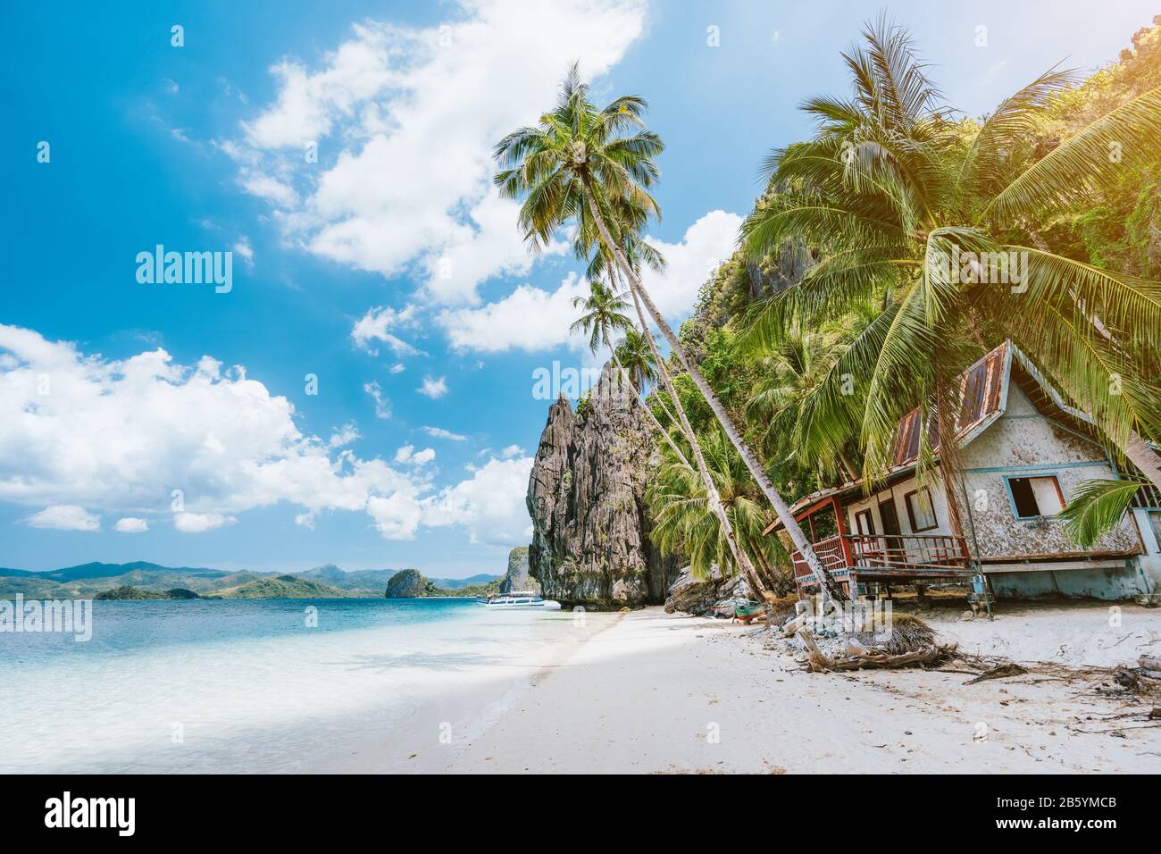 Vacation holiday on Palawan - El Nido island hopping tour. Lonely deserted hut under palm trees, cliff rocks in background. Stock Photo
