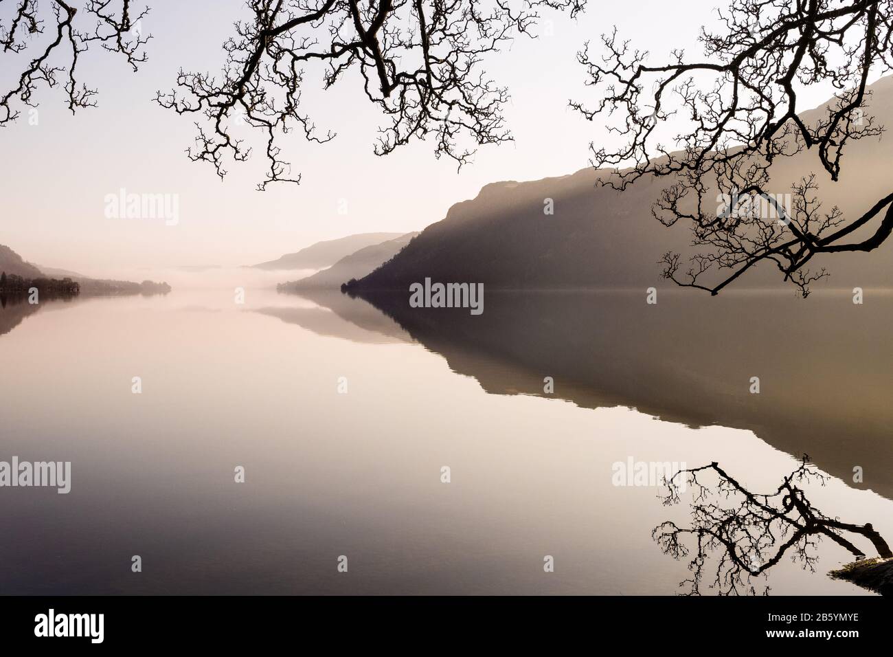 Hills and trees reflected in the water on a calm morning on Ullswater in the Lake District National Park, Cumbria, UK Stock Photo