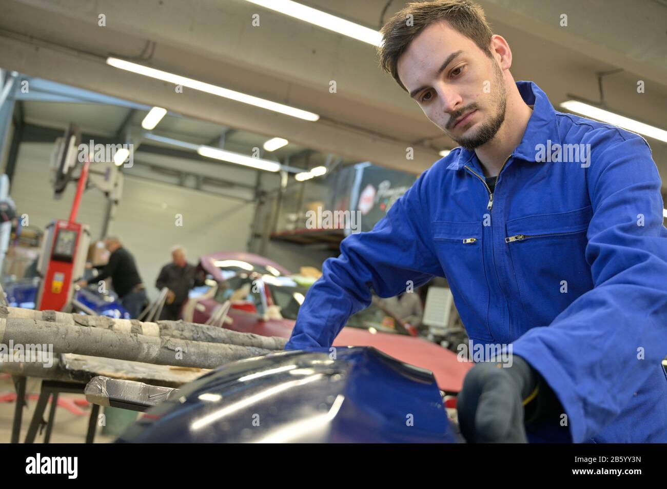 Apprentice working on car engine in workshop Stock Photo