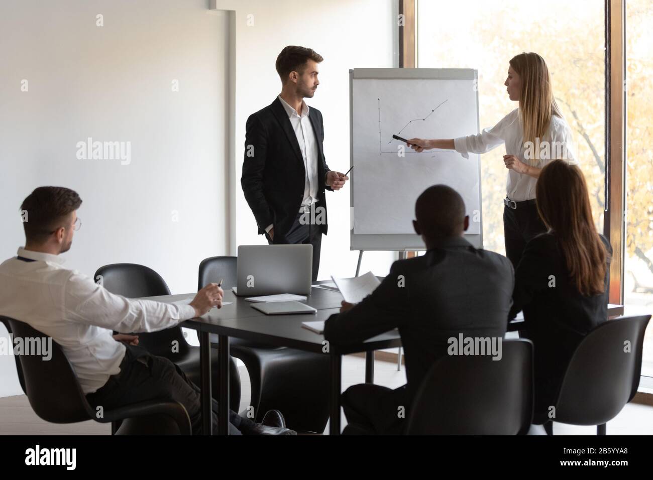 Multiracial team of employees listening to male and female presenters. Stock Photo