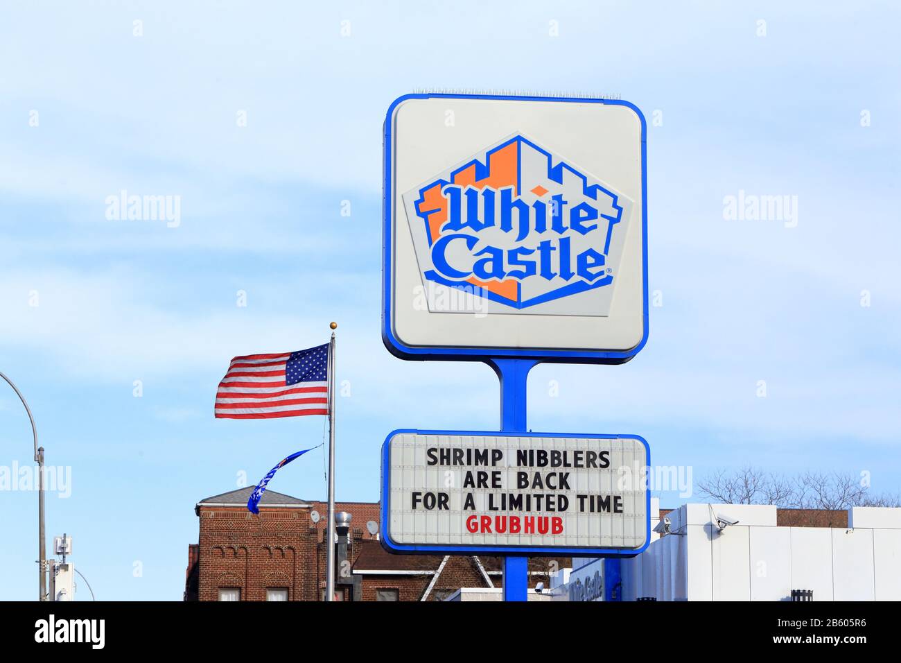A White Castle sign on a pole against a blue sky and American flag. Stock Photo