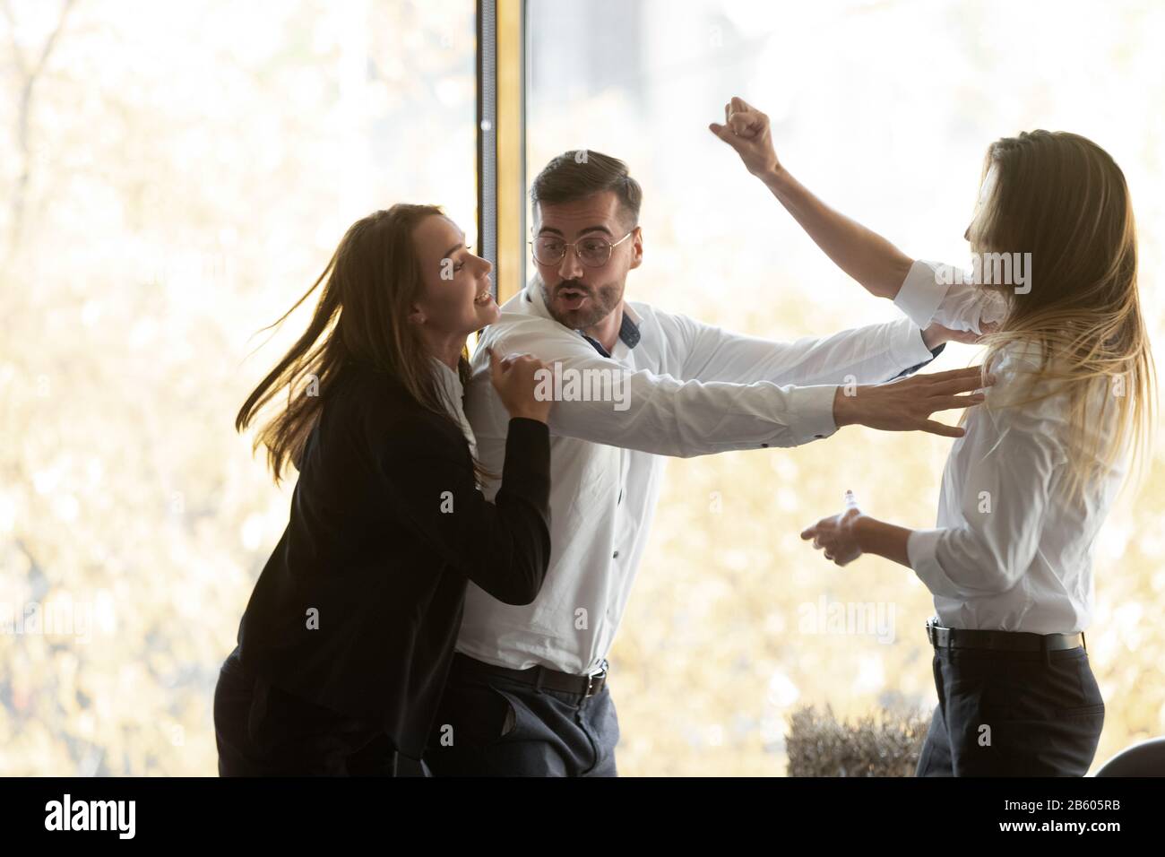Millennial businessman setting apart two aggressive fighting female colleagues. Stock Photo