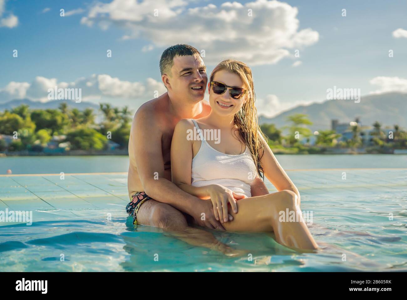 Luxury resort swimming pool. Happy couple tourists relaxing in holiday retreat on summer travel vacation enjoying ocean background Stock Photo