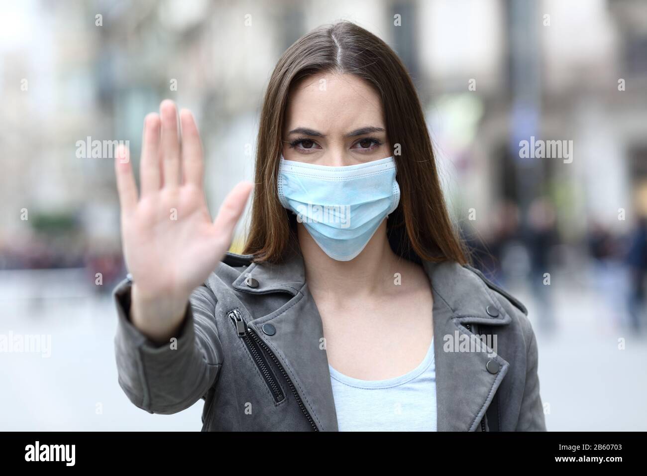 Front view portrait of a serious girl doing stop sign gesture with protective mask on city street Stock Photo