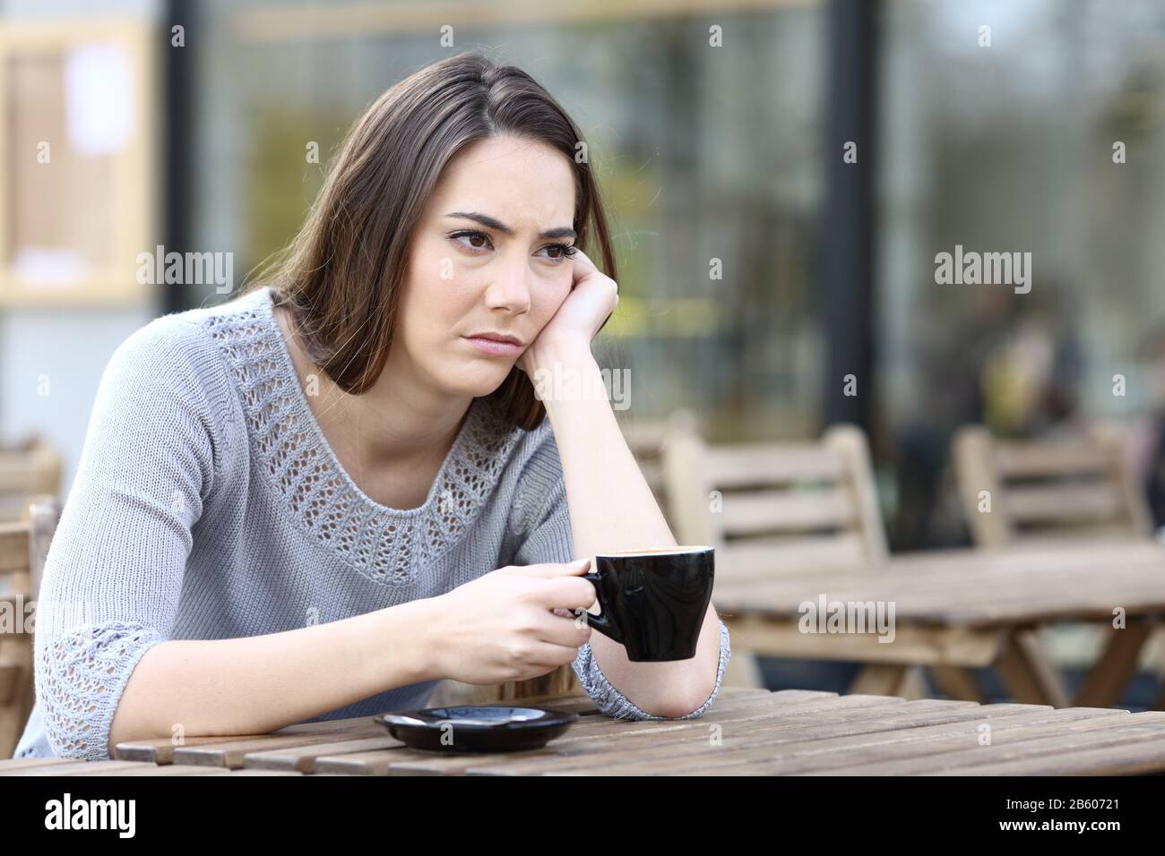 Sad young woman looking away holding a cup of coffee on a restaurant terrace Stock Photo