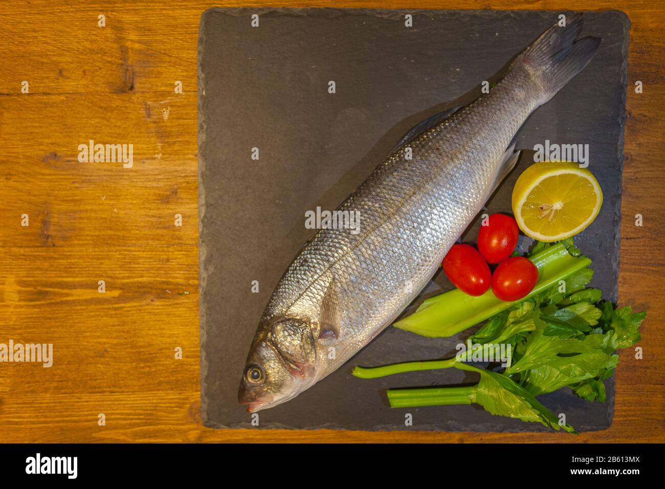 Slate dish with sea bass, lemon, celery and tomatoes Stock Photo