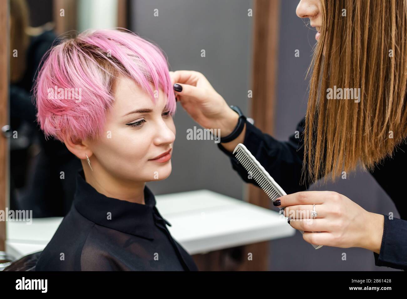 Hairdresser checks short pink hairstyle of young woman in hair salon