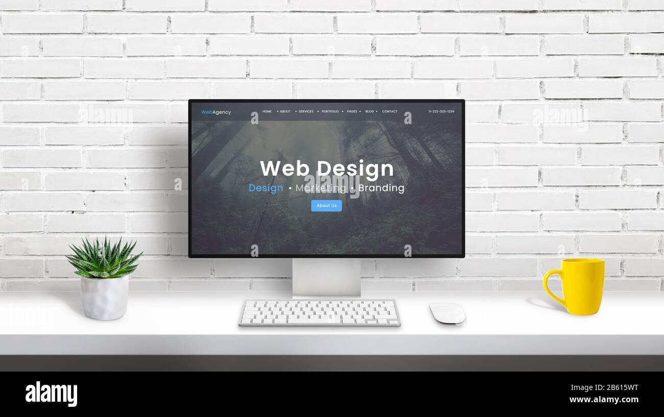 Web design studio concept with computer display and web design agency web page. clean desk with plant, keyboard, mouse and coffee mug. White brick wal Stock Photo