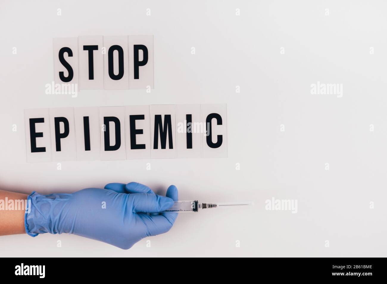 The words STOP EPIDEMIC on a gray background and a gloved hand with a syringe. Stock Photo