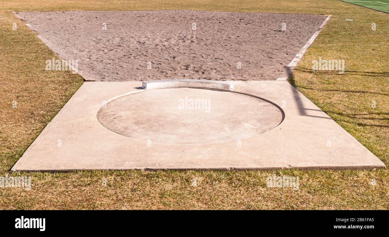 A hammer throw circle with sand in front of it on an athletic field