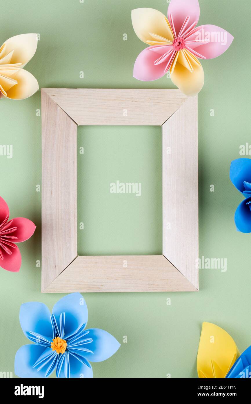 multicolored paper flowers around wooden frame on green background