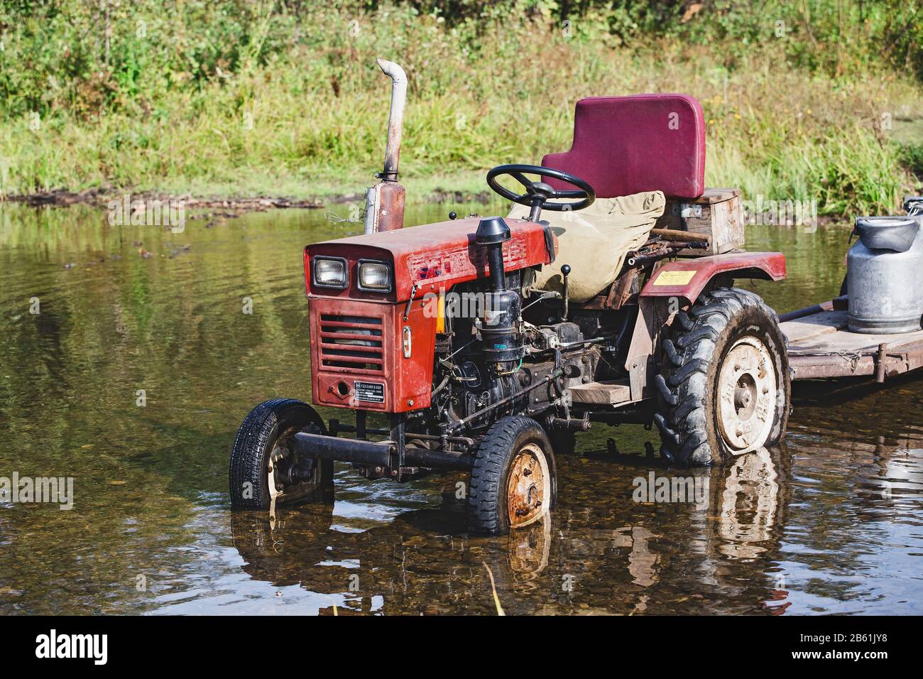 01 SEPTEMBER 2017, NIKOLAEVKA VILLAGE, BASHKORTOSTAN, RUSSIA: Old red tractor in water near the shore of the river Stock Photo