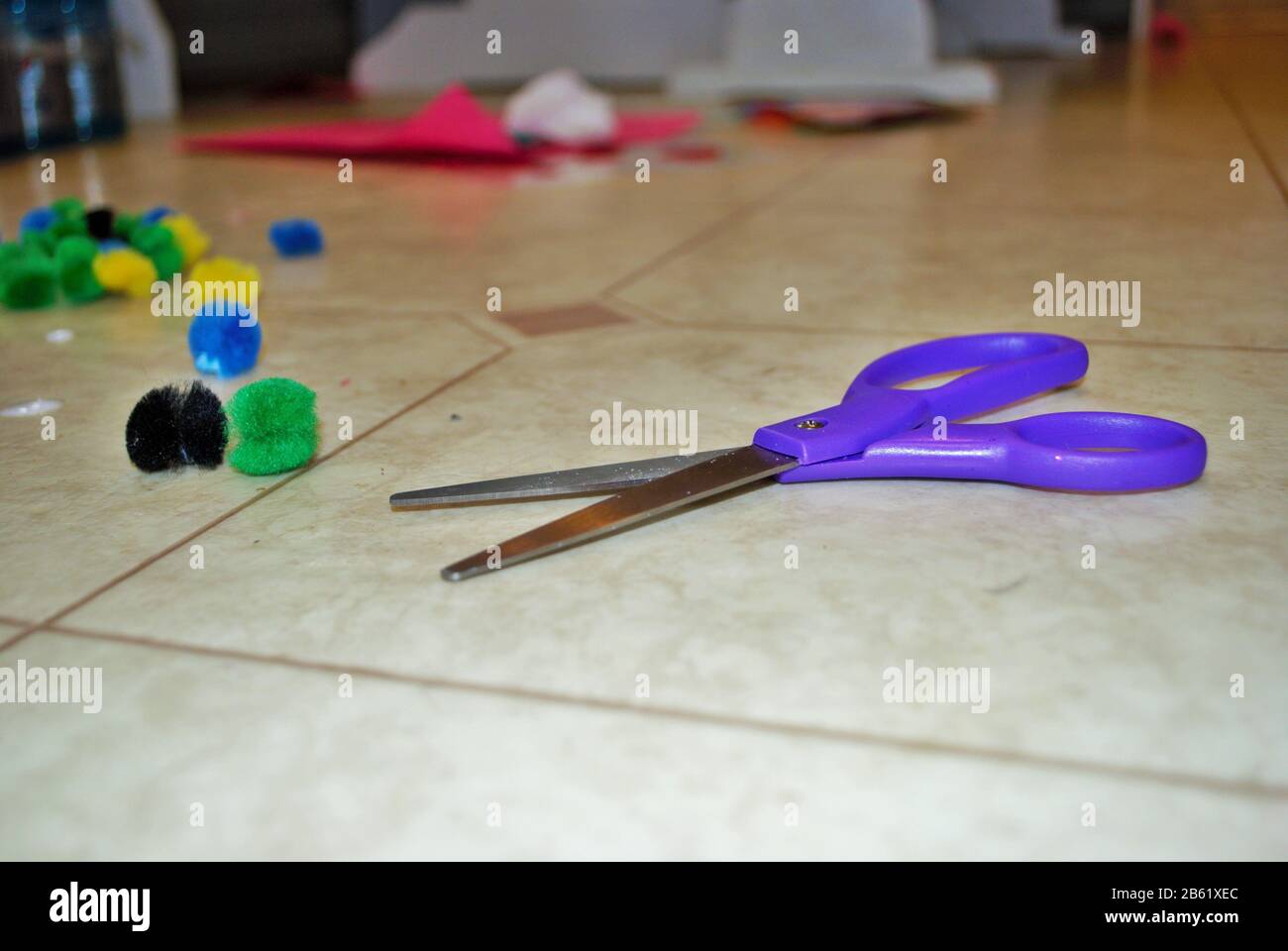 Multi colored cotton balls glue and scissors on a linoleum floor during