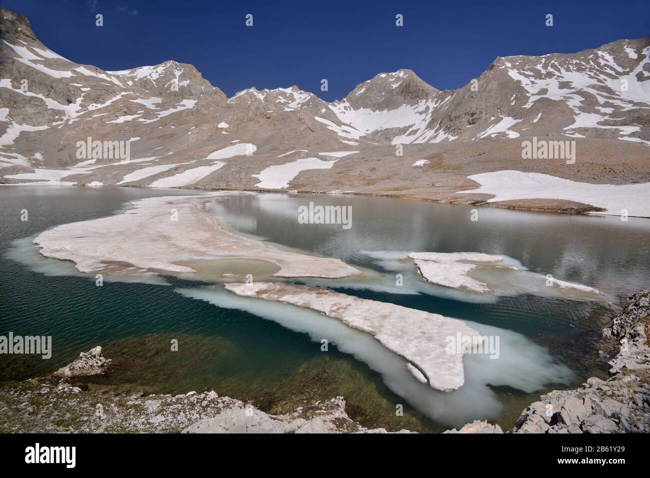 Karagol table land with lake against bright blue sky background. Ice cakes float on water. Turkey, Aladaglar or Anti-Taurus Mountains. Stock Photo