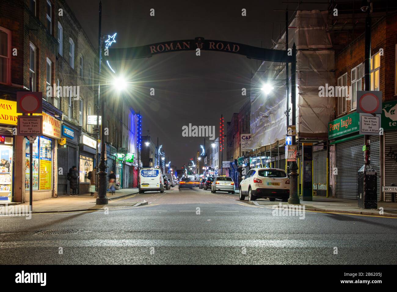 London, England, UK - January 2, 2020: Pedestrians walk past the shops and resturants of Roman Road in London's East End at night. Stock Photo