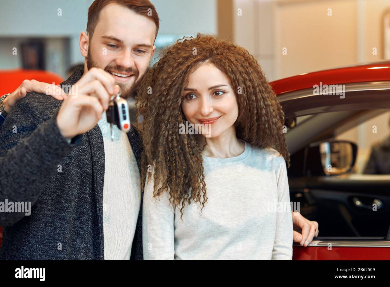 young couple has bought a car, close up photo. man presenting a car for his woman. close up photo. red car in the background of the photo Stock Photo
