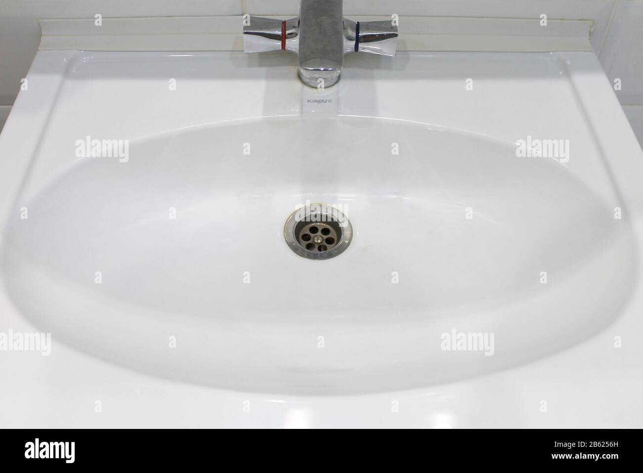 White ceramic washbasin with oval bowl, drain and gray tap in stainless steel. Stock Photo