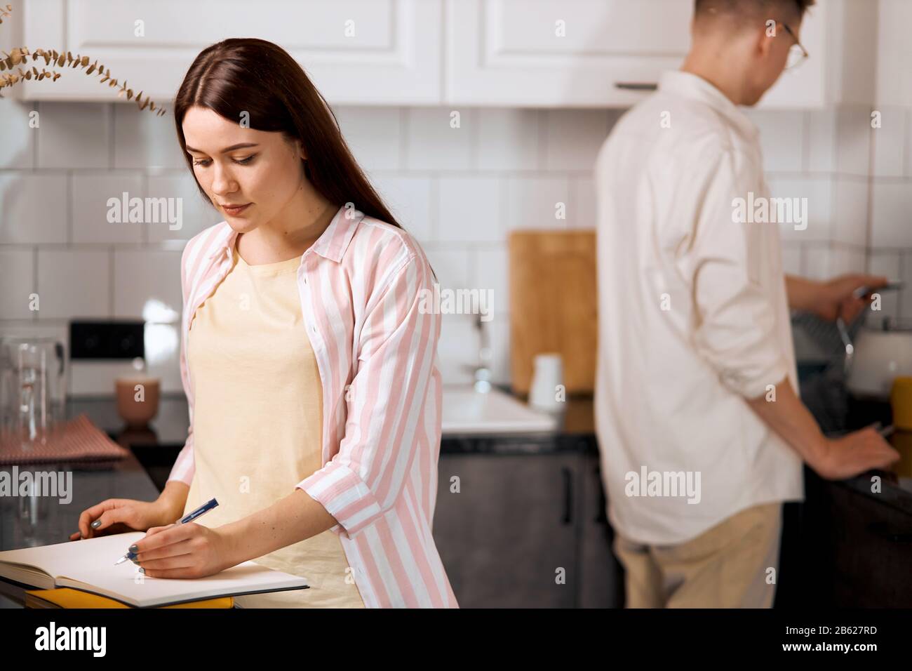 young brown-haired woman writing recipe while her husband going to drink tea, close up photo. lifestyle, spare time, free time Stock Photo