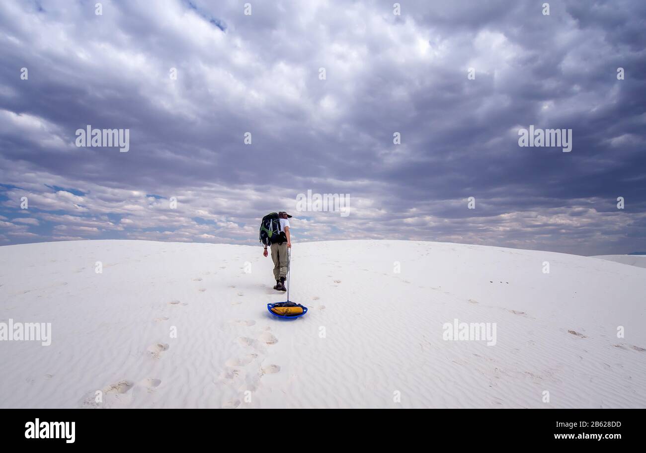 In White Sand National Park, my husband and I planned to have a camping in wilderness. He is dragging our gear to the site. Stormy weather in distance. Stock Photo