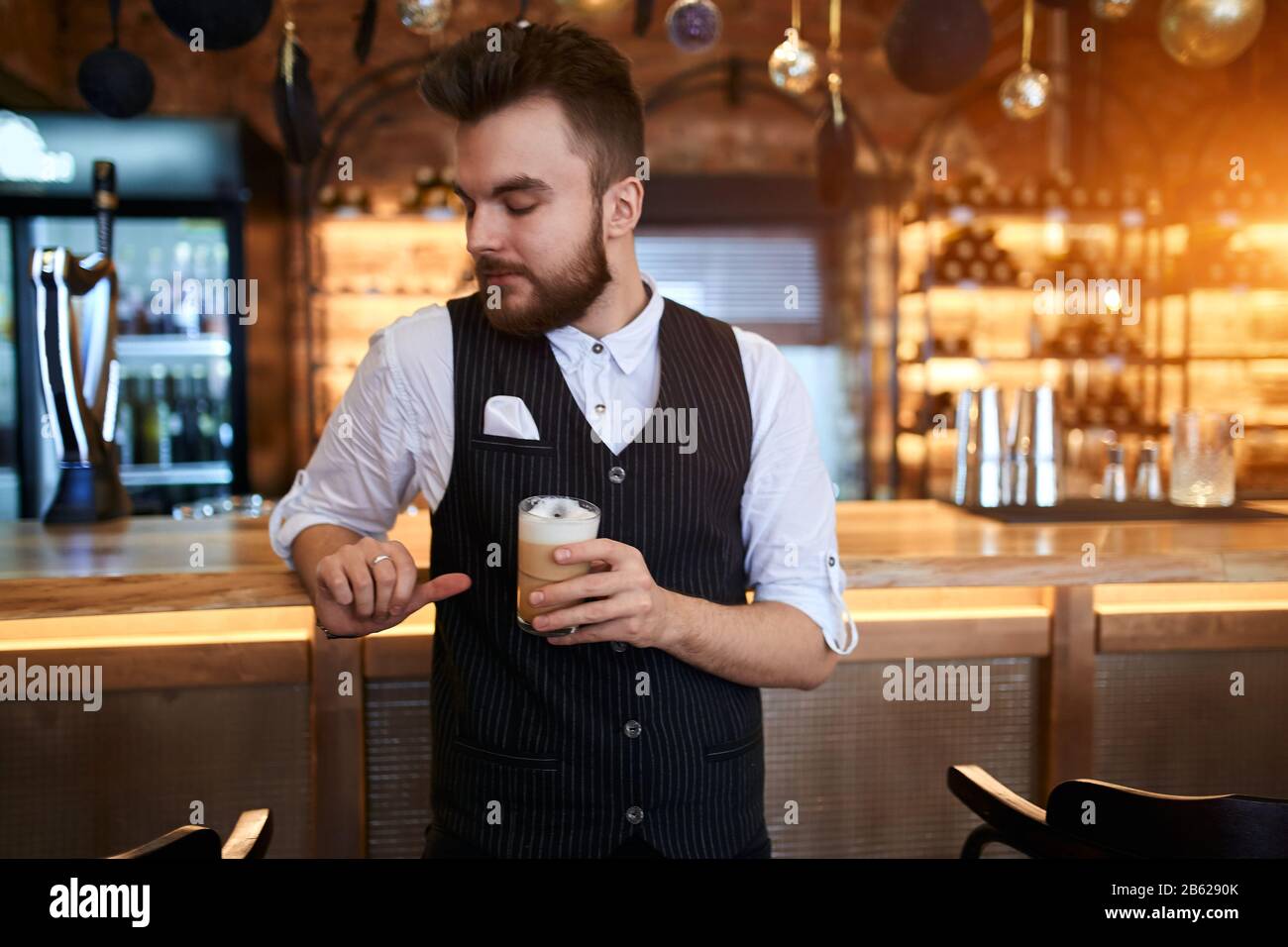 young barista holding glass and looking down wile standing in front of the table. close up photo Stock Photo