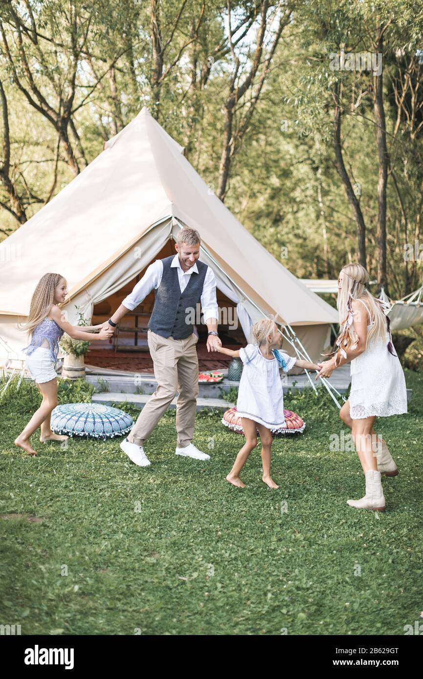 Young stylish family with children have fun in a park. Father, mother and daughters dancing in nature together, holding hands. Family dancing near Stock Photo